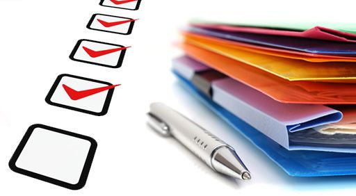 Checklist with red checkmarks in boxes, metallic silver pen, and stack of colorful office folders on a desk.