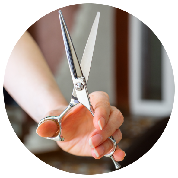 A close up image of hair dresser's hand holding a pair of shears in a salon.